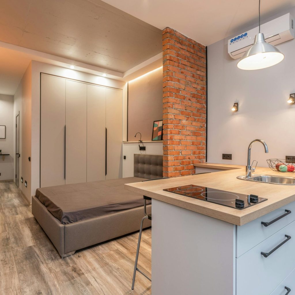 Miniature kitchen with modern appliances and bedroom behind brick partition in small loft style apartment